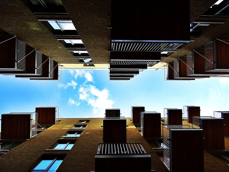 A multi-storey residential building with a concrete facade featuring numerous windows and balconies. The balconies on the left side are decorated with bright yellow horizontal panels, contrasting with